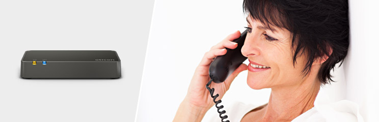 Woman using a corded phone alongside a wireless phone adapter device for hearing assistance.