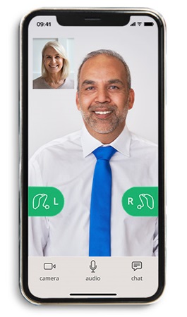 Smartfon wyświetla wideorozmowę na białym tle, osoba w koszuli i niebieskim krawacie omawia kwestie aparatów słuchowych (zielone ikony ’L’ i ’R’).