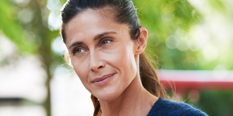 Mujer al aire libre con un audífono detrás de la oreja, rodeada de un fondo verde y desenfocado.
