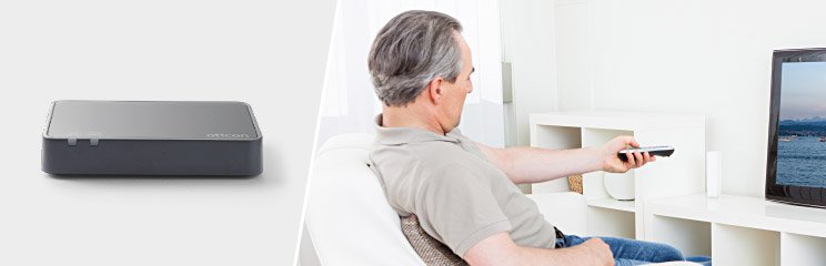 Homem a ver TV com adaptador de áudio Oticon.