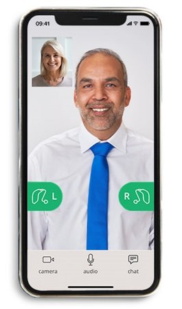 Smartfon wyświetla wideorozmowę na białym tle, osoba w koszuli i niebieskim krawacie omawia kwestie aparatów słuchowych (zielone ikony ’L’ i ’R’).