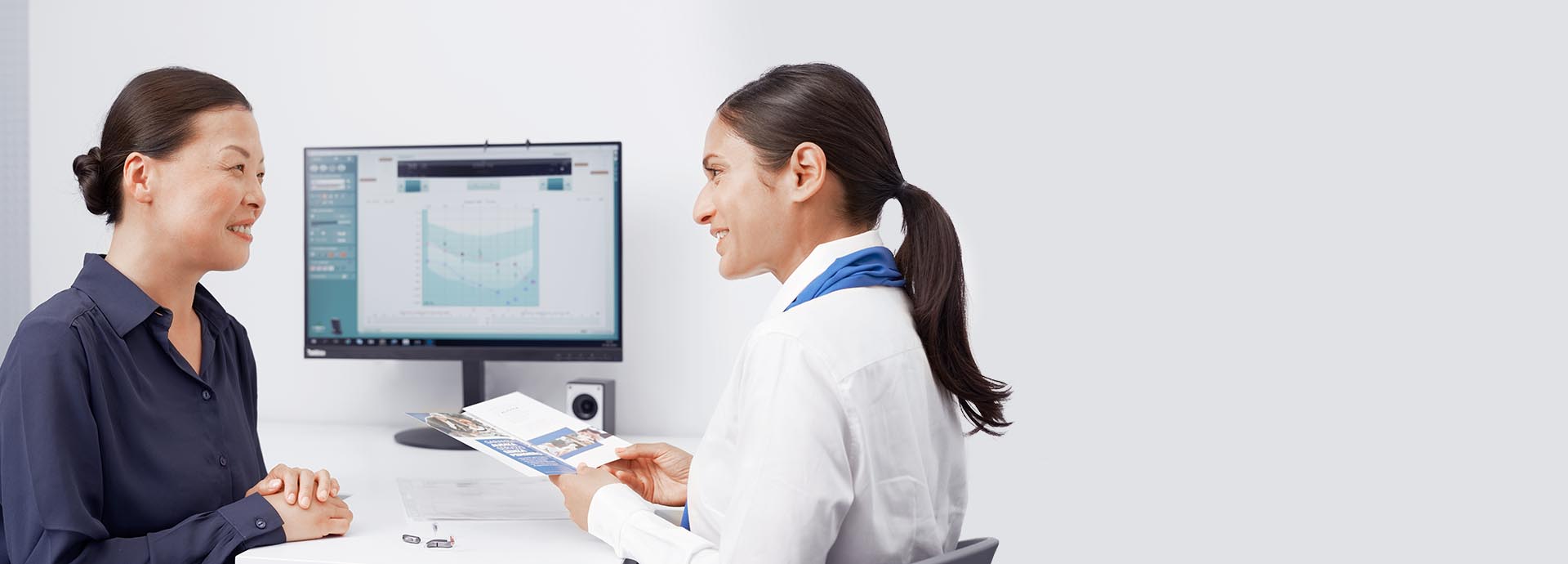 Audika hearing care expert consulting a woman with a hearing test result displayed on a monitor.