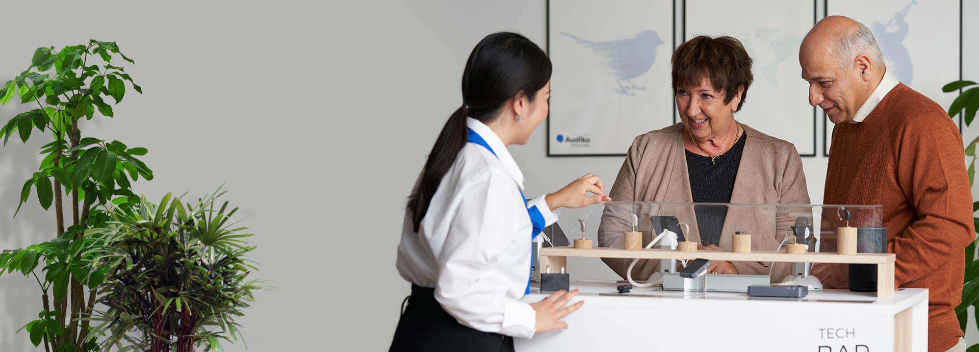 Clinician assisting a couple in selecting hearing aids at a display counter