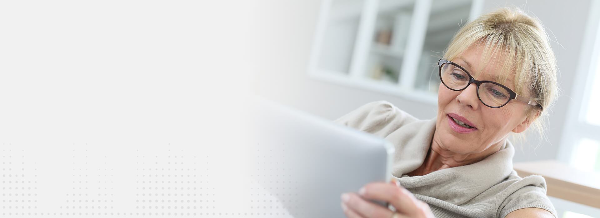 Une femme, lisant une tablette tactile, est assise dans un intérieur lumineux avec des étagères floues en arrière-plan. La scène illustre une ambiance calme et technophile. Aucune marque ou texte visible.
