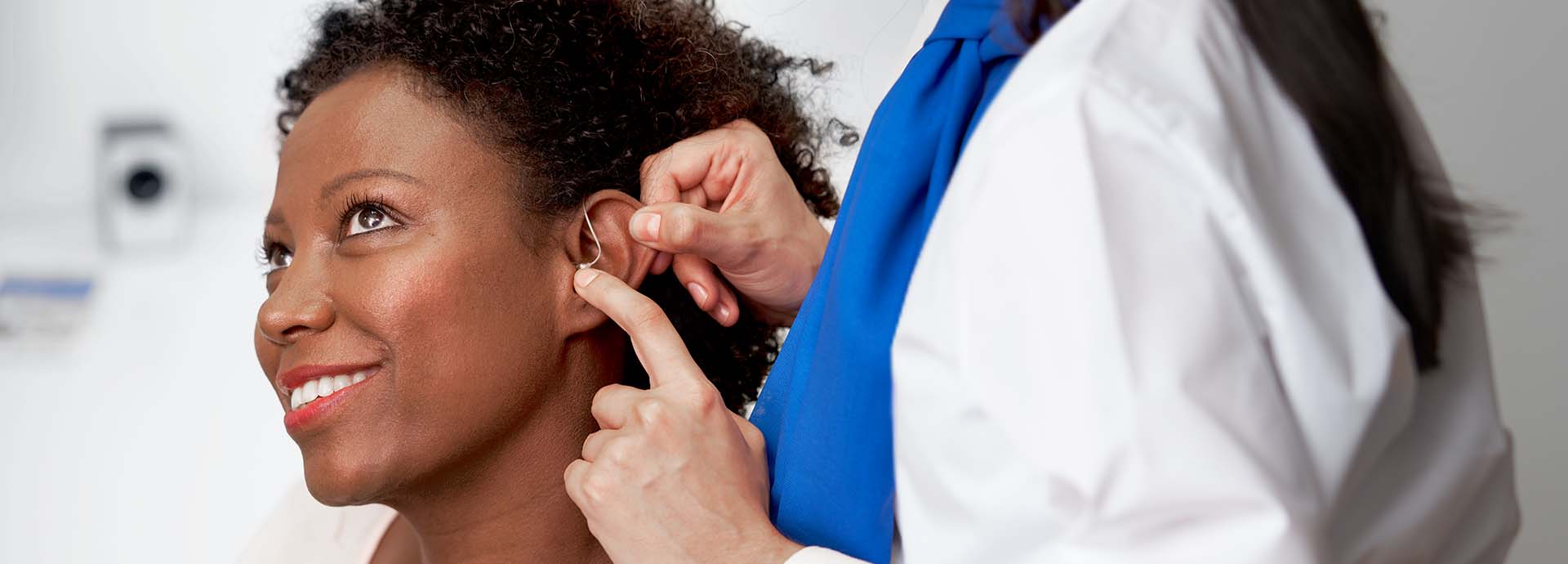 Hearing care professional fitting a hearing aid behind a woman's ear.