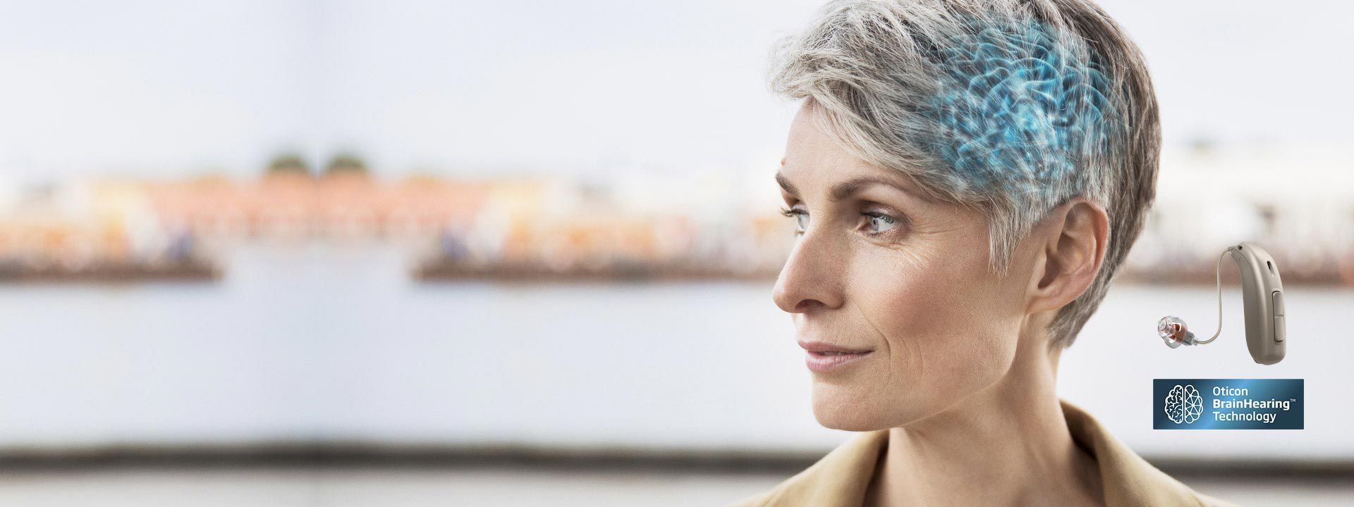 Mulher de cabelo grisalho com cérebro destacado em azul, ao lado de aparelho auditivo com tecnologia BrainHearing da Oticon.