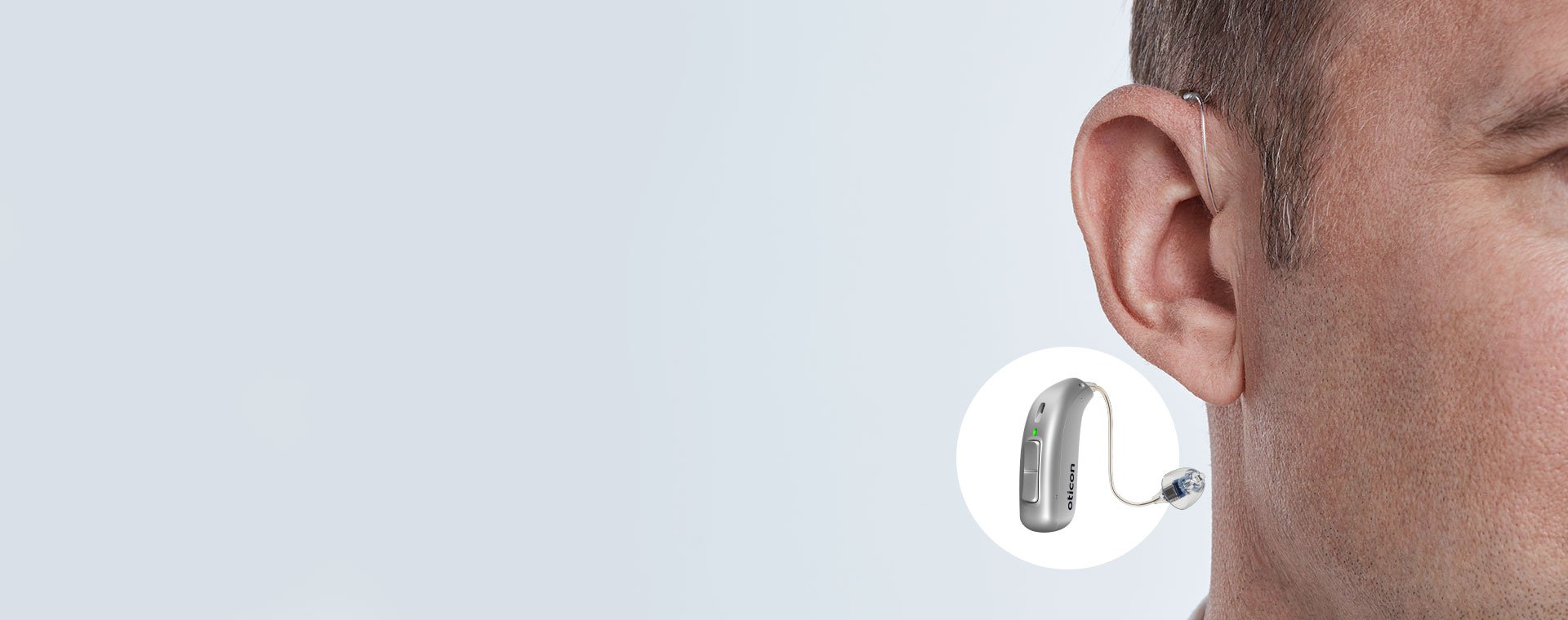 Hearing aid fitted discreetly behind the ear with close-up of the device and its features.