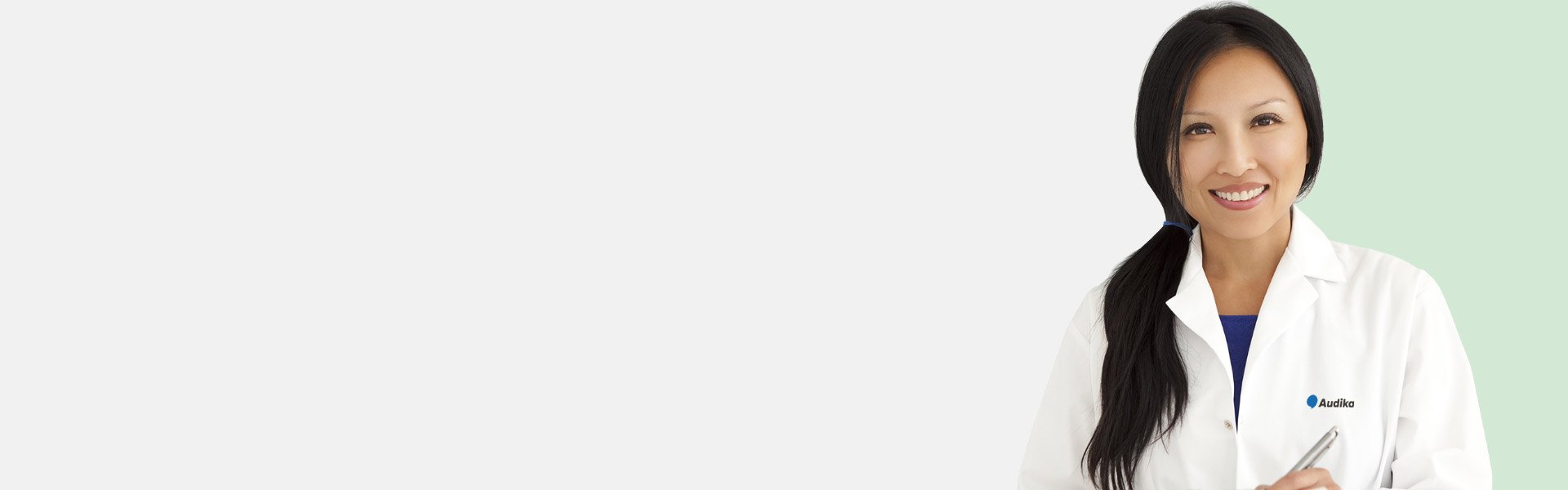 Une audioprothésiste Audika en blouse blanche tenant un stylo.