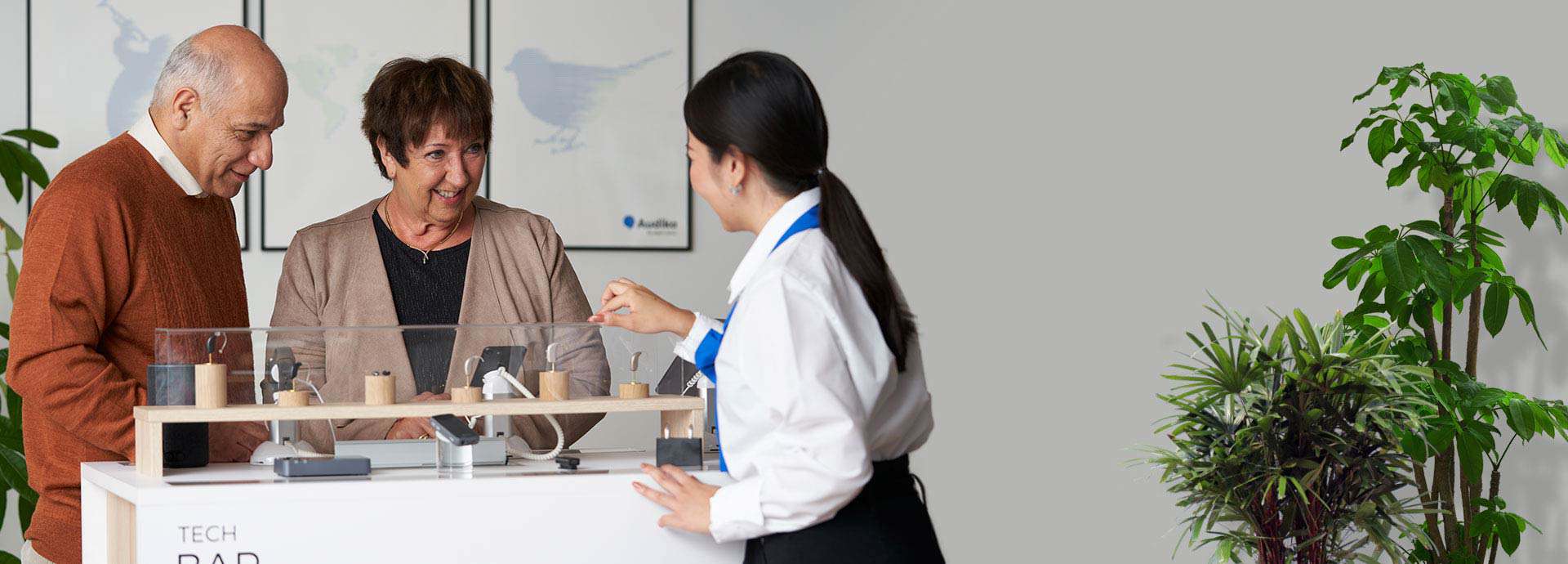 Coppia che prova accessori per apparecchi acustici assistita da un’operatrice.