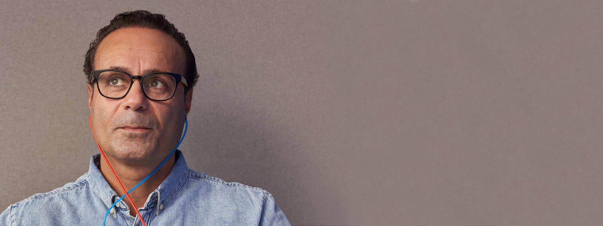 Uomo che indossa una camicia di jeans durante un test dell’udito con auricolari colorati.