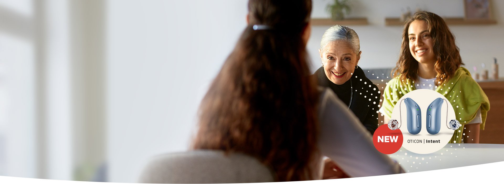 A woman with long brown hair faces two blurred individuals seated across a desk in a bright, modern setting. A promotional graphic in the foreground highlights 'NEW Oticon Intent' blue hearing aids with decorative elements.