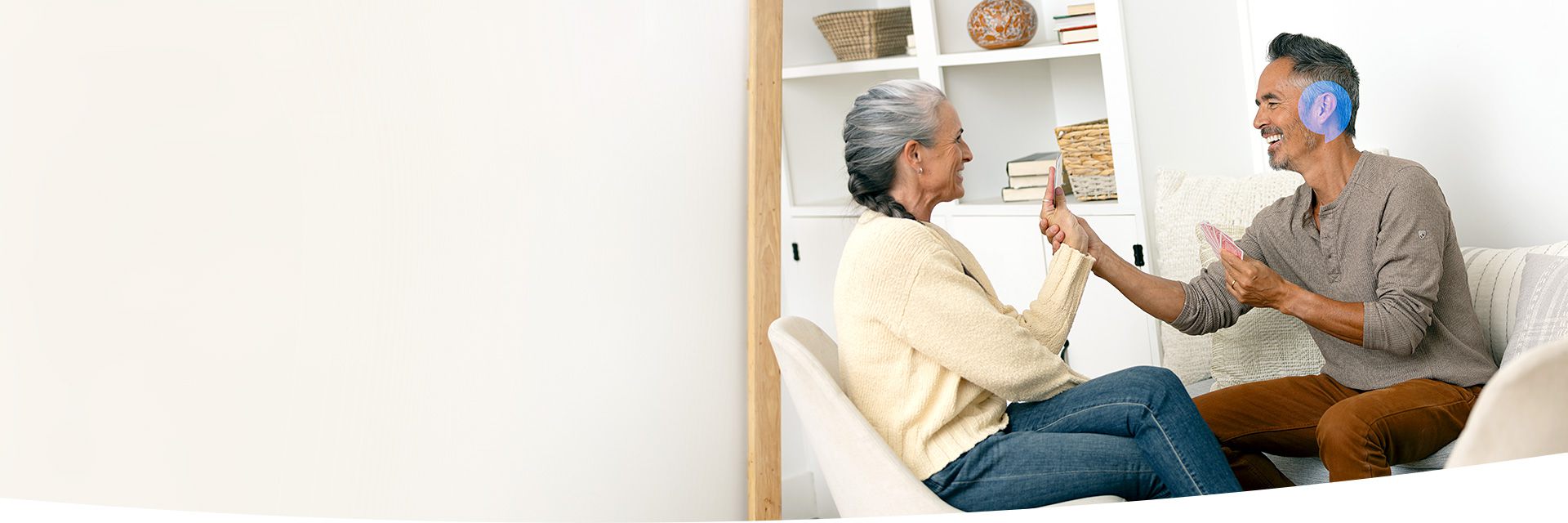 A couple talking while seated in a living room, with the man’s ear accented in blue to highlight hearing focus.