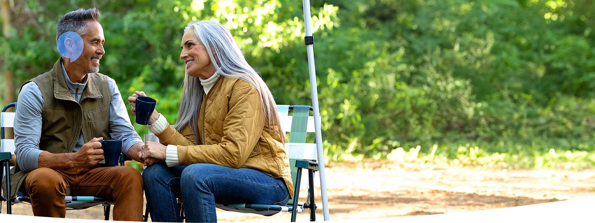 Senior couple holding hands and chatting while enjoying coffee outdoors in a park setting.