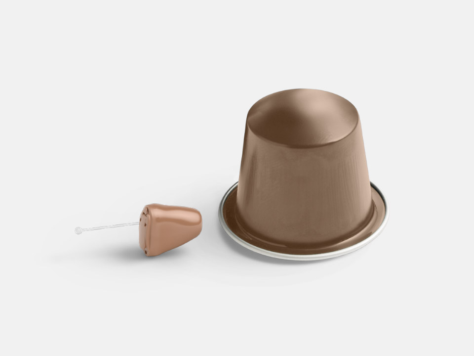 Appareil auditif intra-auriculaire beige placé à côté d’une capsule de café marron sur fond blanc