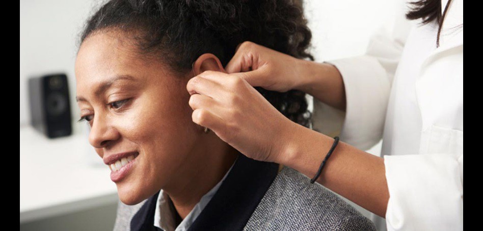 Woman receiving professional hearing aid adjustment.