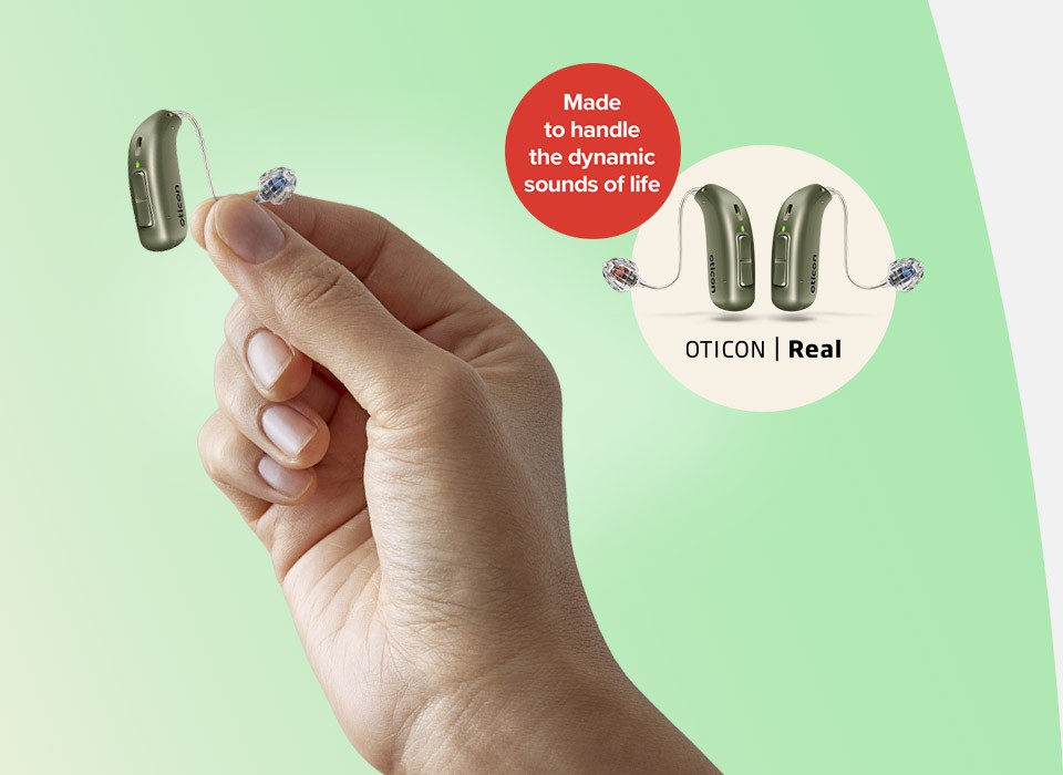 A hand holds an Oticon Real hearing aid featuring a sleek receiver-in-canal design. A circular inset shows two hearing aids with the text: 'Made to handle the dynamic sounds of life. OTICON | Real.' The background fades from light green to white.