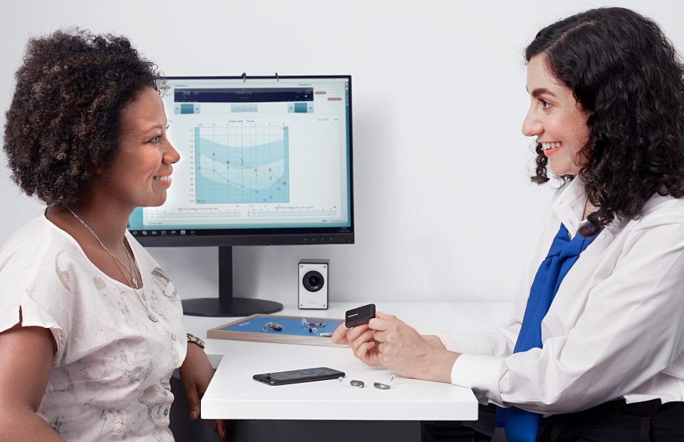 Woman consulting with a hearing specialist while viewing an audiogram on a computer screen and exploring hearing aid options.