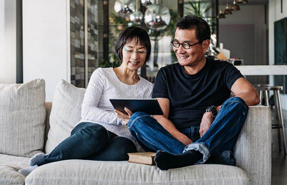 Casal sentado no sofá em uma sala de estar moderna, olhando juntos para um tablet.