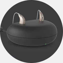 Charging pod with two modern hearing aids placed on top.