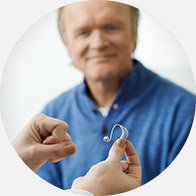 Une audioprothésiste montre une aide auditive à un patient en consultation