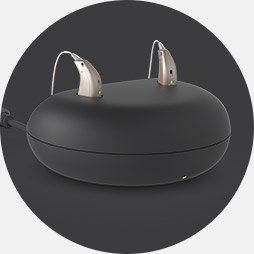 Charging pod with two modern hearing aids placed on top.