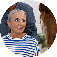 Older woman wearing hearing aids, seated indoors, engaging with a hearing care professional.