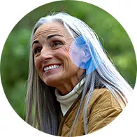 Femme âgée aux cheveux gris tenant ou ajustant un appareil auditif en plein air