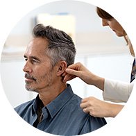 Een audioloog plaatst een gehoorapparaat achter het oor van een man in een moderne hoorkliniek. De ruimte heeft een lichte en professionele uitstraling zonder zichtbare merknamen.