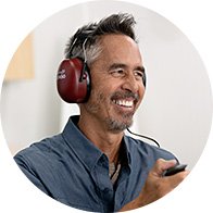 Een persoon draagt rode gehoor-testkoptelefoons, houdt een knop in de hand en ondergaat een gehoortest in een hoorcentrum. De achtergrond is licht en neutraal.