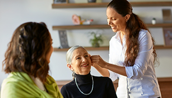 hearing care professional fitting a hearing aid on an older woman while another woman observes