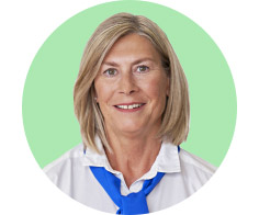 Person med lyst skulderlangt hår iført hvid skjorte og blå halstørklæde står foran en mintgrøn baggrund. Ansigtet er sløret. Ingen tekst eller synlige høreapparater er identificerbare.