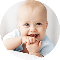 Smiling baby wearing a light blue outfit, leaning forward with hands near the mouth.