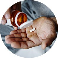 Mão de pessoa segurando um comprimido enquanto despeja de um frasco de medicamento.