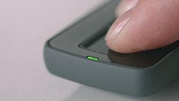 [OPT] Finger pressing a button on a hearing aid remote control with a green indicator light.