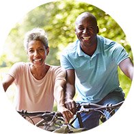 Casal andando de bicicleta ao ar livre em um dia ensolarado, cercado por árvores.
