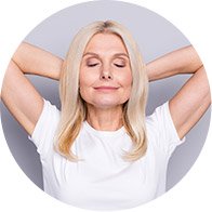 Femme blonde souriante avec les mains derrière la tête, portant un t-shirt blanc.