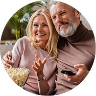 Casal sentado no sofá, segurando pipocas e um telecomando.