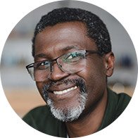 Homme souriant portant des lunettes, avec un arrière-plan flou.