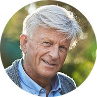 Een oudere man met grijs haar draagt mogelijk een onzichtbare gehooroplossing, gefotografeerd buiten in een zonnige, groene omgeving. 