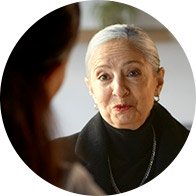 Eine Person mit kurzen, silbergrauen Haaren, möglicherweise in einer Hörklinik, sitzt gegenüber einer anderen Person. Der Hintergrund zeigt eine unscharfe, helle Umgebung ohne spezifische Details. Kein Text erkennbar.