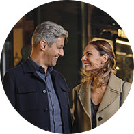 Een man en een vrouw praten terwijl ze wandelen in een stedelijke omgeving met nachtverlichting. Beiden dragen nette kleding; gehoorapparaten of audiologische elementen zijn niet duidelijk zichtbaar.