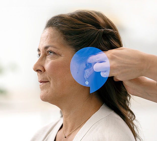 Image shows woman having a hearing aid placed behind her ear