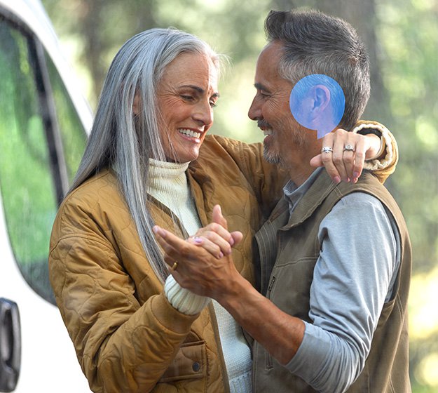 Older couple dancing outdoors with a focus on the man’s hearing aid.