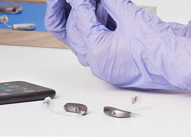 Gehoorapparaten op tafel naast smartphone en handen met paarse handschoenen