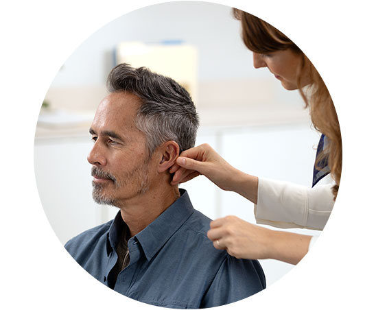 Un audioprothésiste ajuste un appareil auditif sur l’oreille d’un patient dans un cabinet moderne.