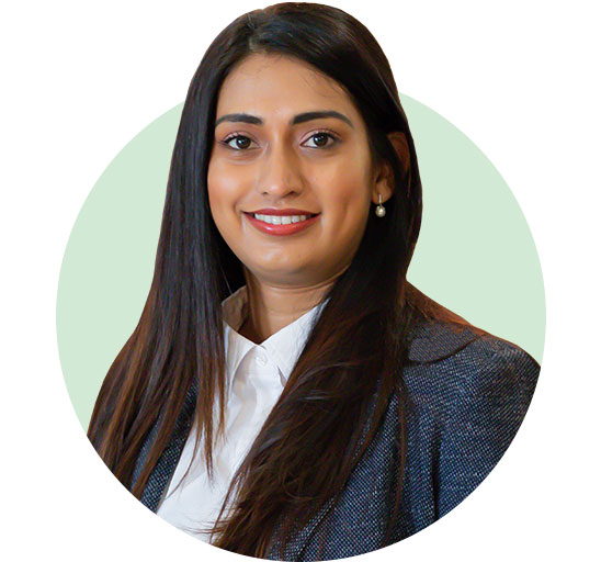 Uma mulher com cabelos longos e lisos veste camisa branca e blazer cinza em um fundo verde claro. Seu rosto está desfocado, e não há texto ou identificação visível.