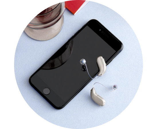 Gehoorapparaten naast een smartphone op een lichtblauwe achtergrond.
