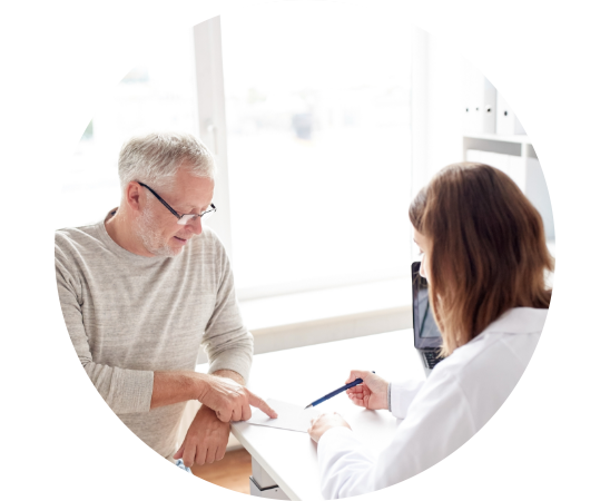 Un uomo anziano consulta un'audioprotesista in un centro acustico, seduti a un tavolo con documenti. Sullo sfondo, una finestra luminosa illumina l'ambiente professionale. 