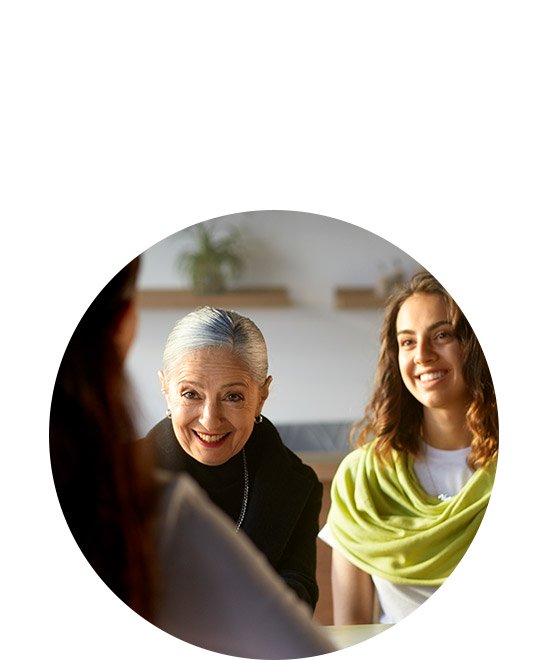 Un grupo de personas está sentado conversando en un entorno interior iluminado y moderno, con estantes decorativos y plantas en el fondo. Las caras están difuminadas. No hay texto visible.