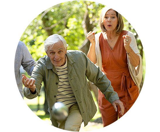 Um homem grisalho usa um paletó brilhante em um ambiente festivo com luzes coloridas. Ao lado, destaque para aparelhos auditivos discretos, ressaltando soluções da Audika para perda auditiva.